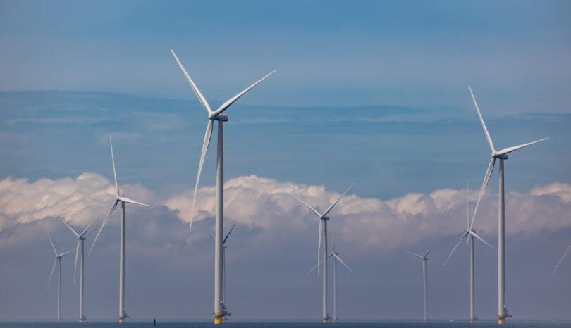 Large wind turbines stand in the ocean. 