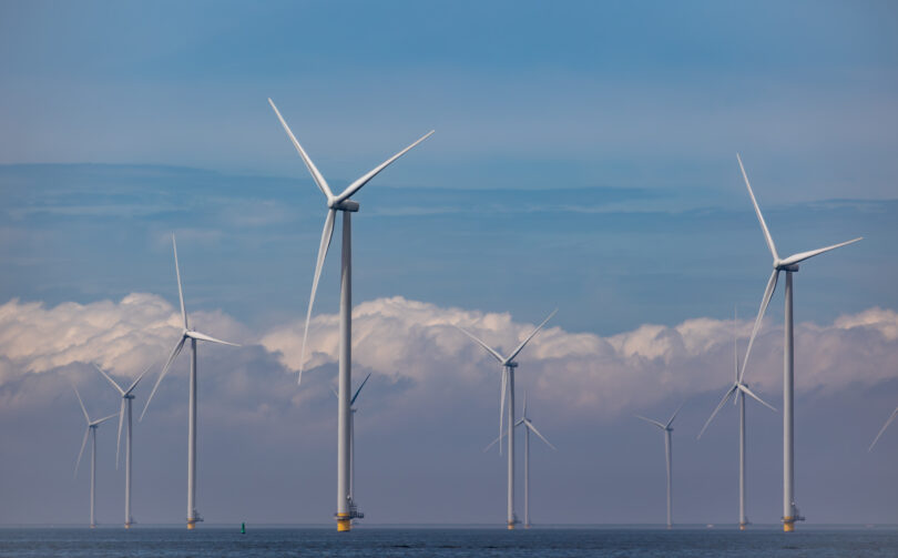 Large wind turbines stand in the ocean. 