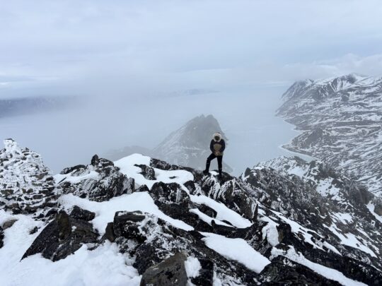 Man stands on top of snow covered mountain peak in the Arctic